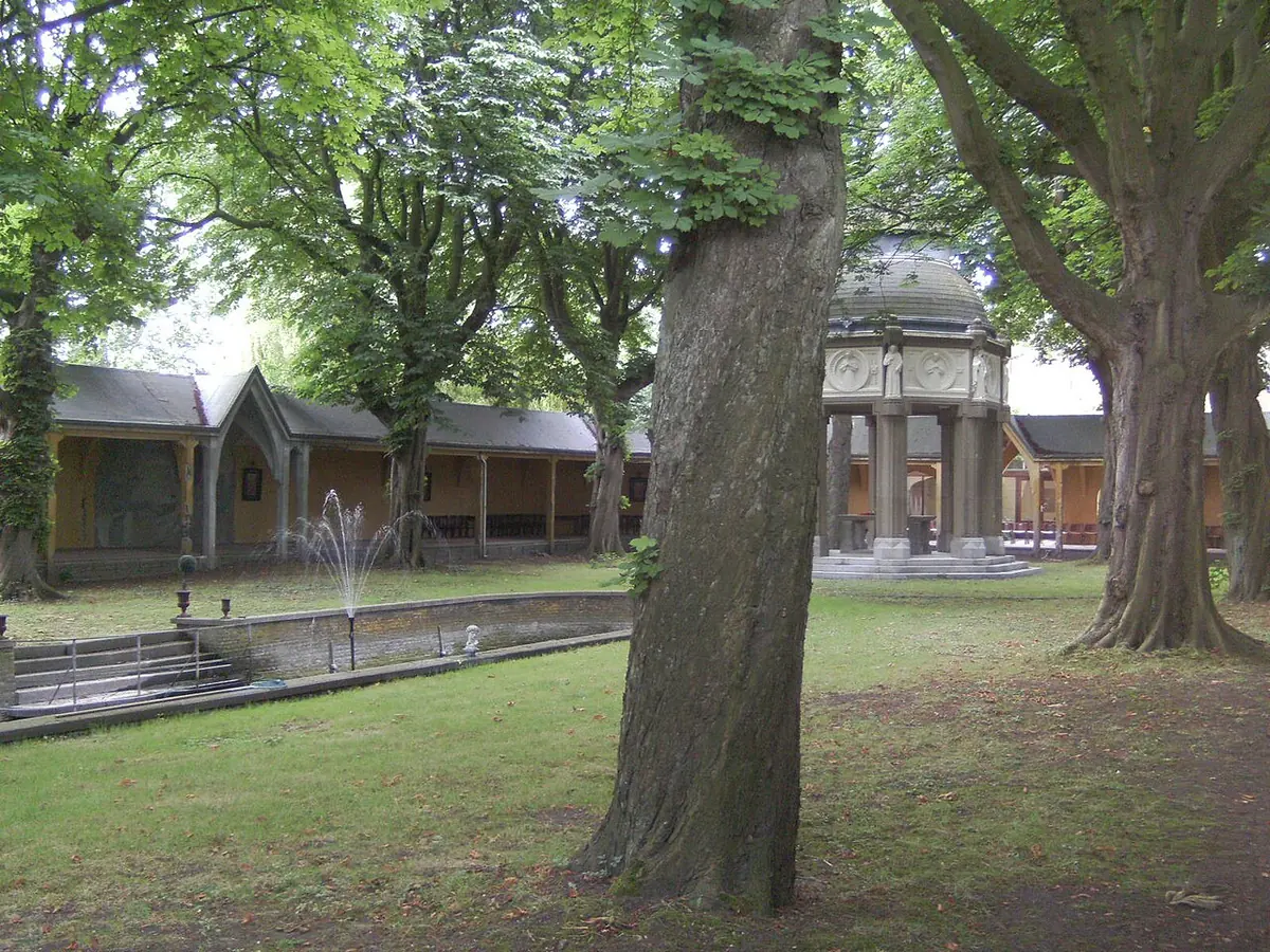 Shaded garden with old trees, a long pond, a domed well house and low open galleries on the martyrs' field in Brielle