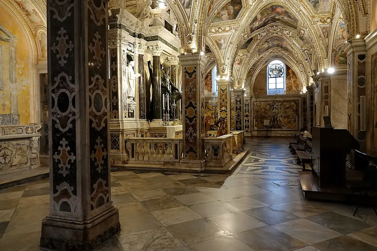 Richly decorated Baroque crypt with inlaid marble pillars, a painted vaulted ceiling and an altar topped by a bronze statue