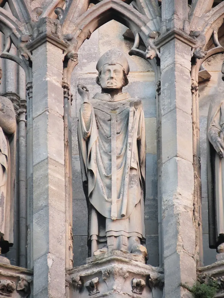 A weathered stone statue of a bishop in miter and chasuble standing in a Gothic niche