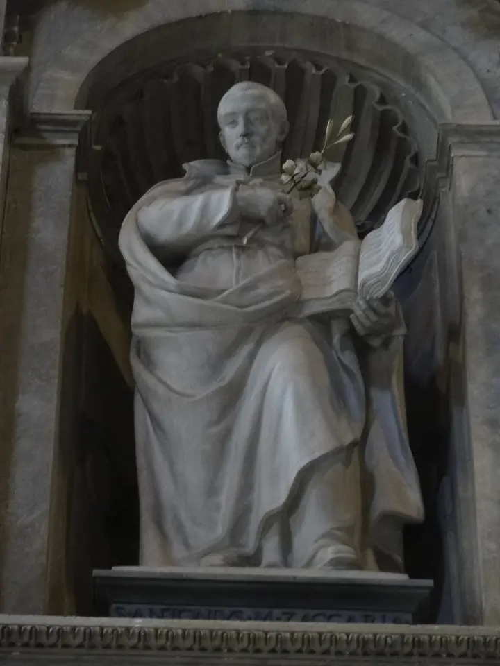 White marble statue of a priest in a flowing cassock holding a lily and an open book, standing in a niche of St. Peter's Basilica