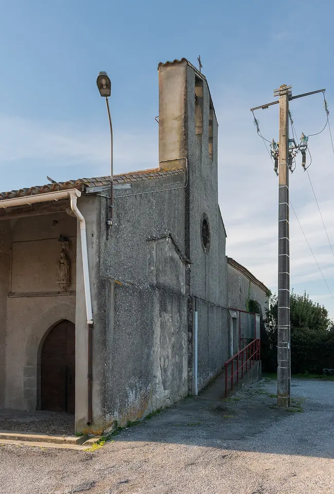 Plain stone village church with a tall narrow bell tower and an arched doorway under a blue sky in southern France
