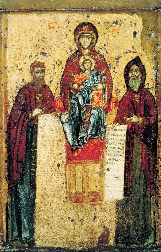 Old painted icon of the Mother of God enthroned with the Christ Child, flanked by two standing monks holding scrolls, on a worn gold background