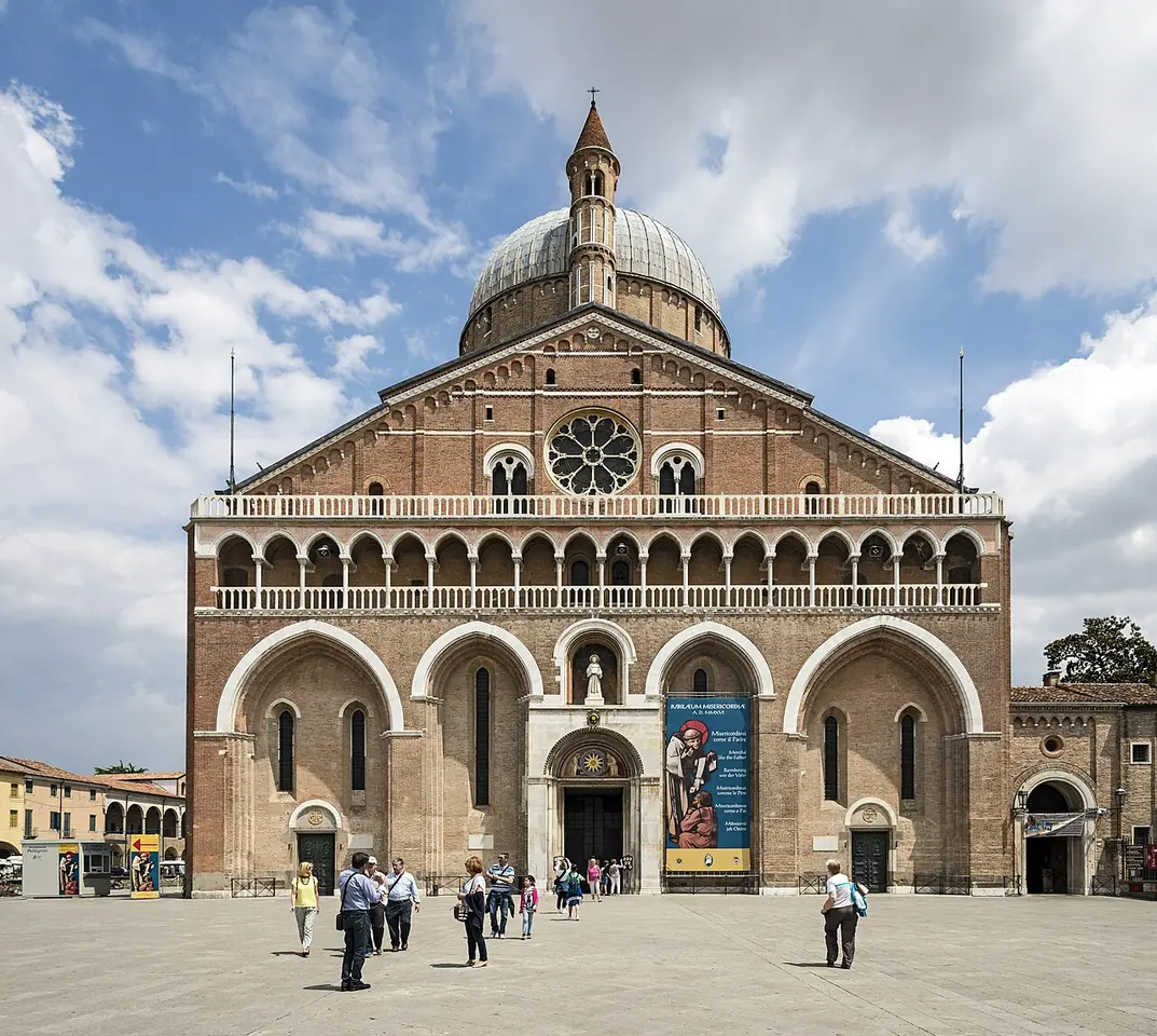 The brick facade of the Basilica of St. Anthony in Padua, with an arcaded gallery, a rose window and domes rising behind, above a wide stone square