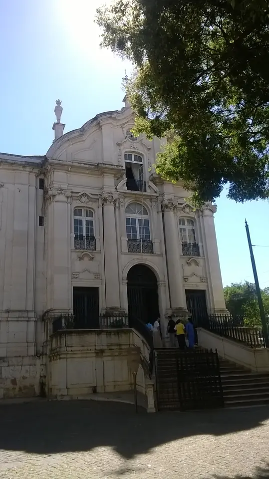 White and gray Baroque facade of the Church of Santo António in Lisbon, with a stairway leading up to the door and trees at the side