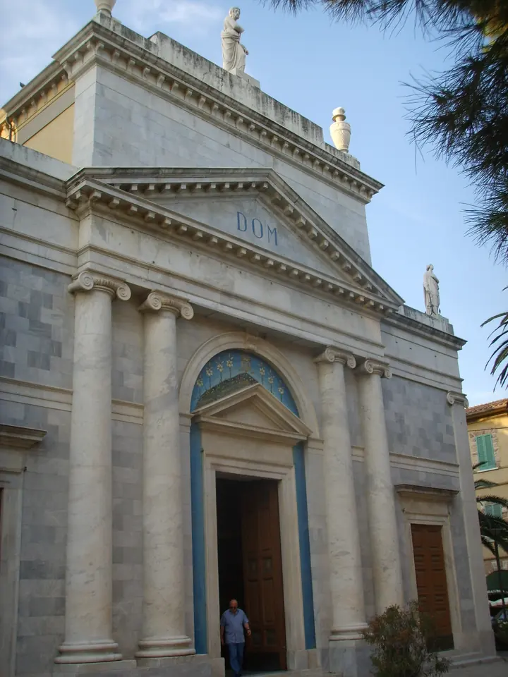 The white neoclassical front of the Church of Sant'Andrea in Viareggio, with tall columns, a triangular pediment and statues on the roofline against a blue sky