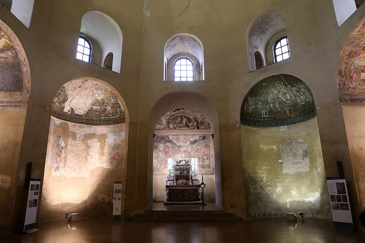 The high octagonal interior of the Chapel of Sant'Aquilino with arched niches, faded early Christian mosaics and the saint's silver urn on the altar in the far niche