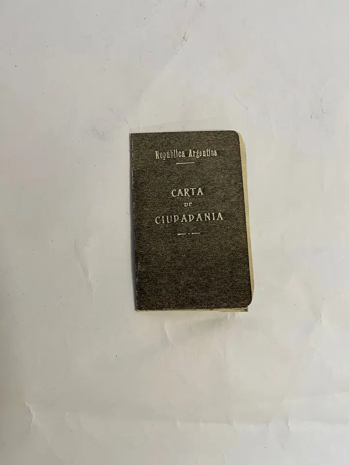 Small worn dark green booklet with the words República Argentina and Carta de Ciudadanía stamped on its cover, lying on a white surface