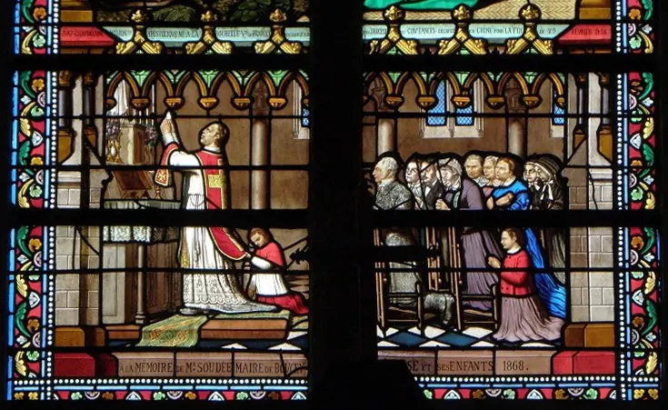 A stained-glass window in two panels showing a priest in red vestments raising the Host at an altar with a kneeling server, while men, women and children kneel at their pews
