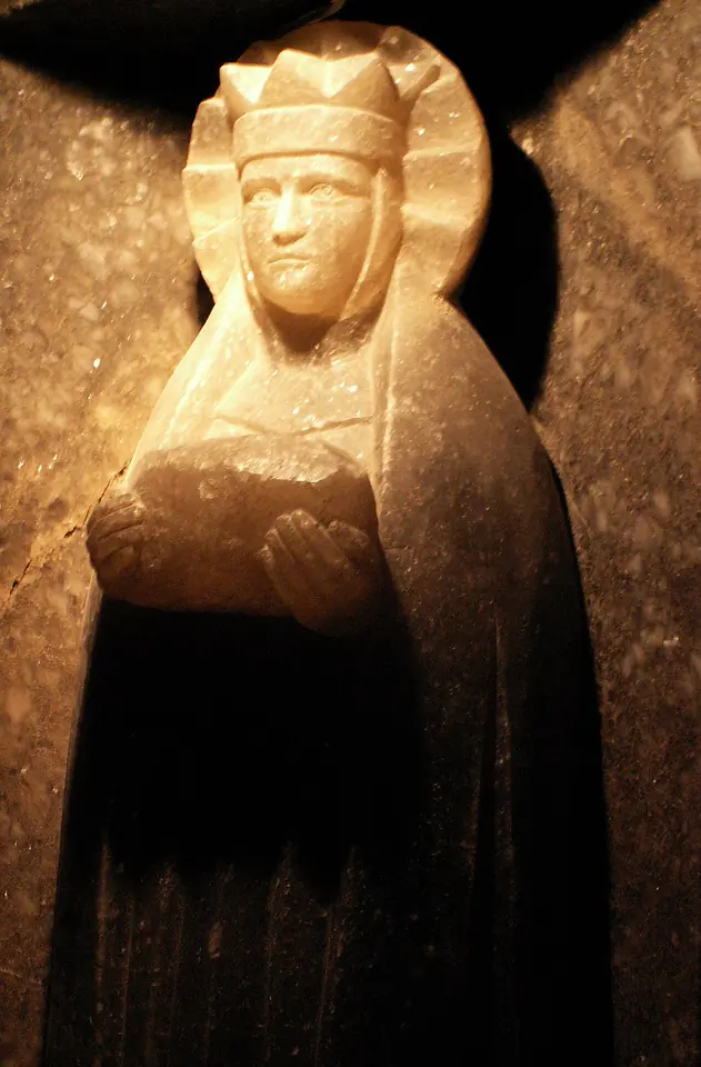 A pale crowned statue of St. Barbara, her hands joined before her, lit warmly from below in a dark chamber of the salt mine