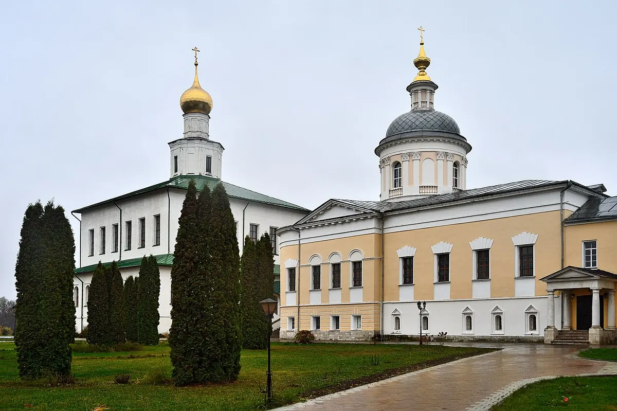Two white and cream churches with gilded and silver domes standing among dark cypress-shaped trees on a lawn