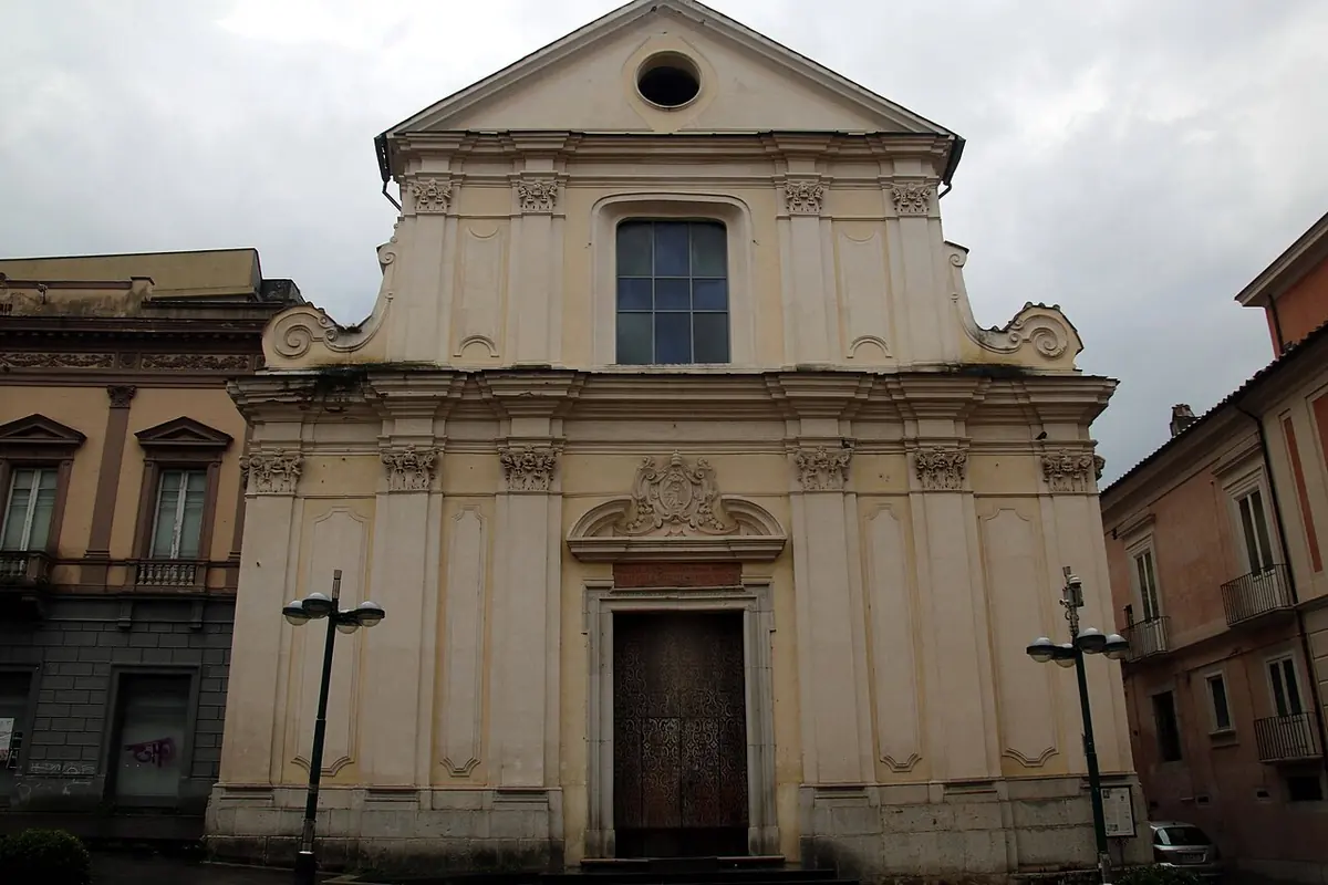 The pale stone facade of the Basilica of San Bartolomeo in Benevento with pilasters, a round window and a single central door, under a cloudy sky