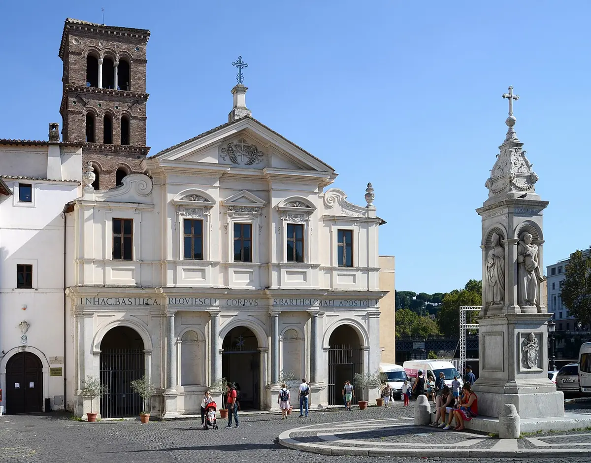 The white Baroque facade and medieval brick bell tower of the Basilica of San Bartolomeo on Tiber Island, with a carved stone column in the square in front