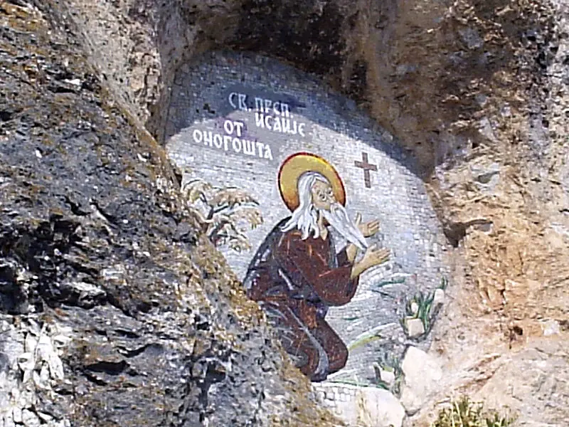 Pilgrims crowding through a small arched doorway topped with a cross into a church cut into the rock