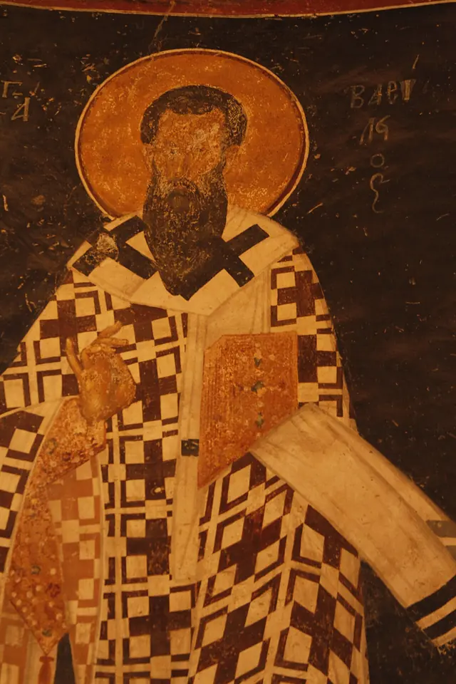 Byzantine fresco of St. Basil with a dark beard and halo, wearing a vestment patterned with crosses and holding a book