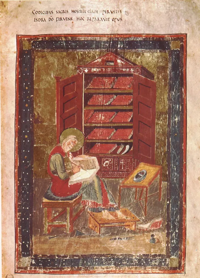 Manuscript painting of a haloed scribe seated on a bench writing in a book on his knee, in front of a red cupboard with open doors full of books