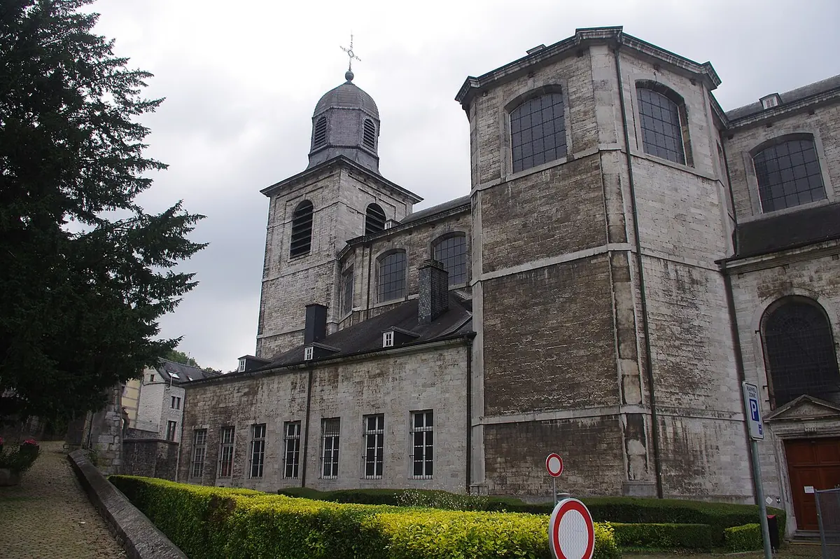 Large gray neoclassical stone church with a square tower and a bell-shaped roof, seen from a garden