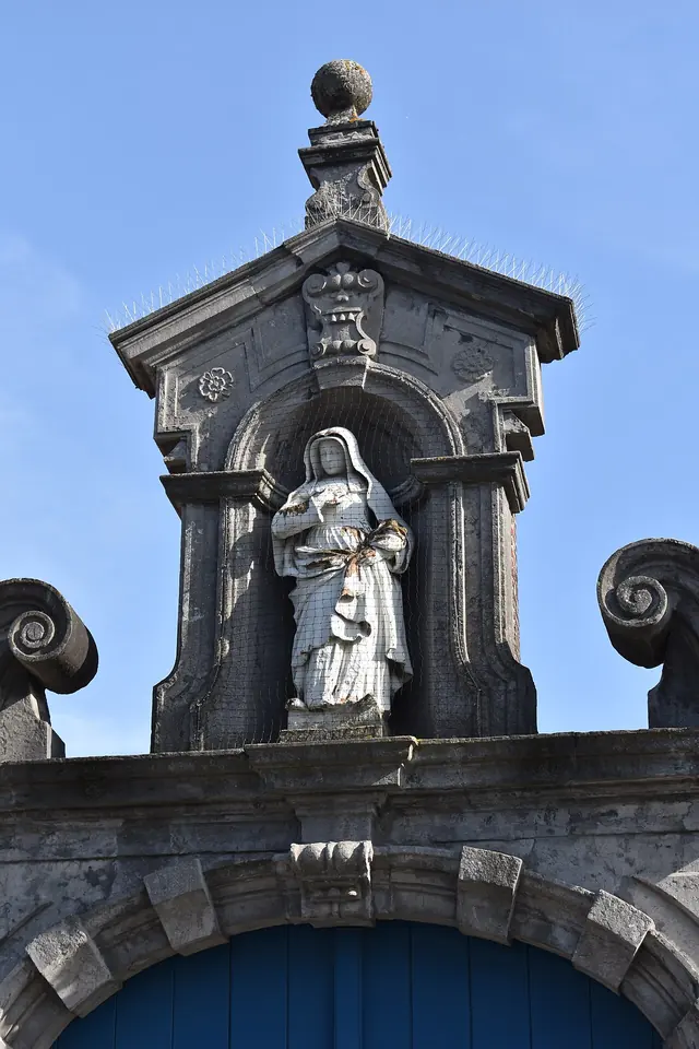 Stone Baroque gateway with a statue of St. Begga in a niche at the top, under a blue sky