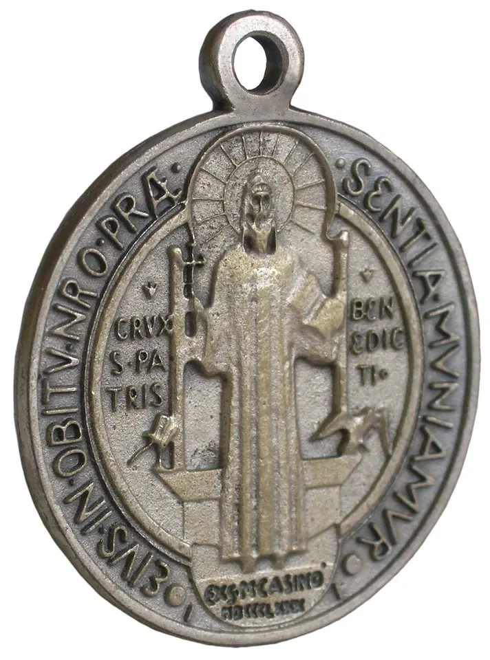 Front of an oval pewter-colored St. Benedict medal with a loop, the saint with cross and Rule, the cup and raven at his sides, and the words Ex S M Casino MDCCCLXXX below his feet