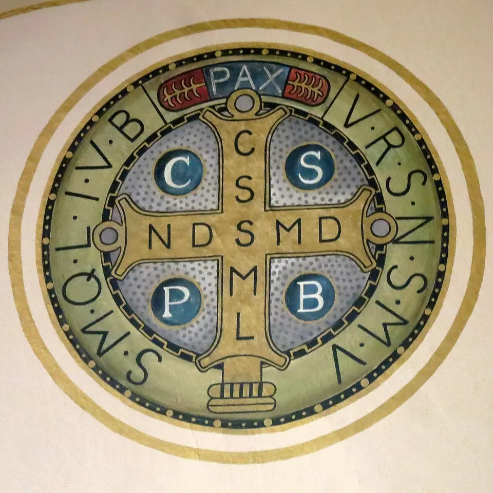 Large painted circle of the back of the St. Benedict medal, a gold cross with the letters CSSML and NDSMD, CSPB in blue roundels, PAX at the top and VRSNSMV SMQLIVB around the rim