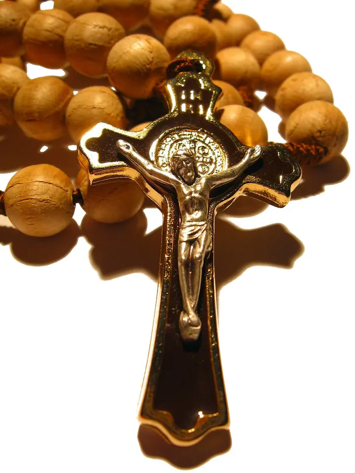 Close-up of a wooden-bead rosary ending in a gold crucifix with a small St. Benedict medal set in the center of the cross