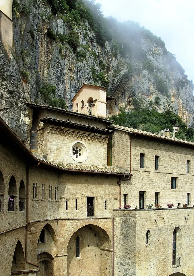 The stone buildings and arcades of the Sacro Speco monastery built into a sheer gray cliff face above Subiaco