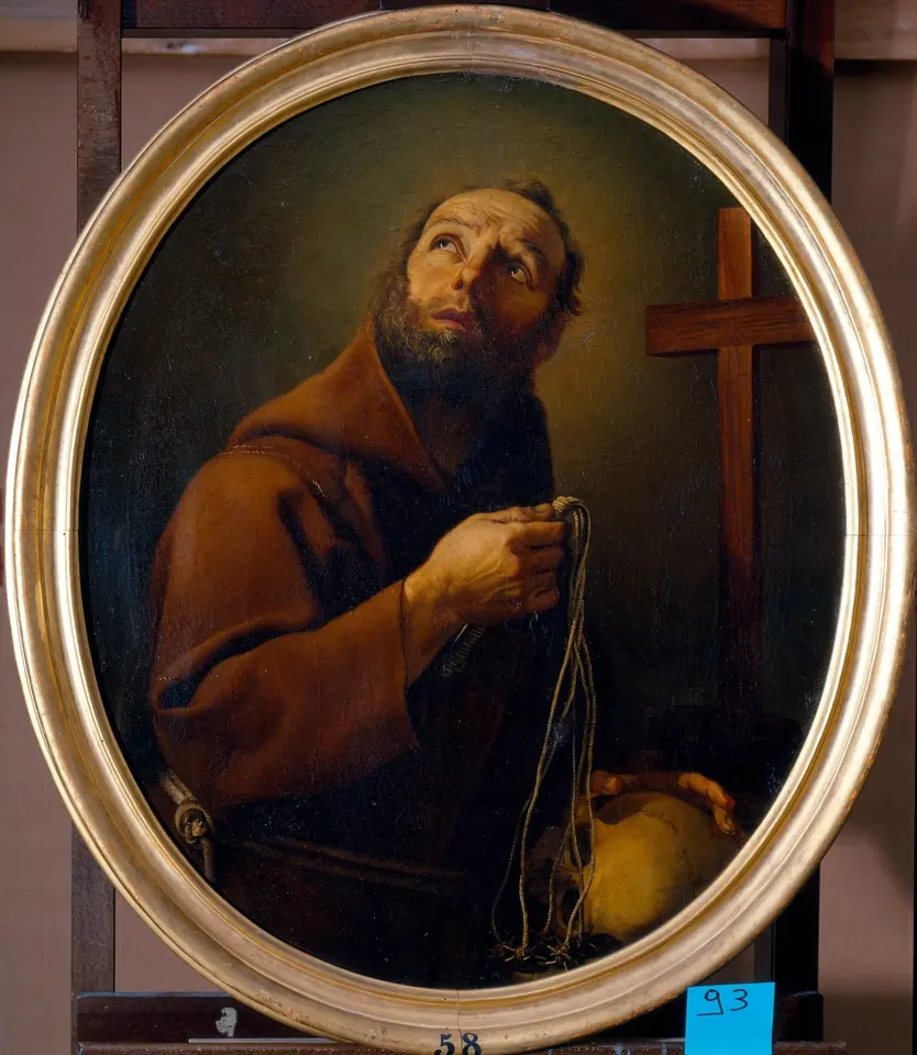 Oval painting of a bearded Capuchin friar in a brown habit looking up to heaven and holding a rosary, with a wooden cross and a skull beside him