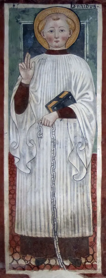 Fresco of a young saint with a halo in a white pleated surplice, holding a book and a chain, raising his hand in blessing