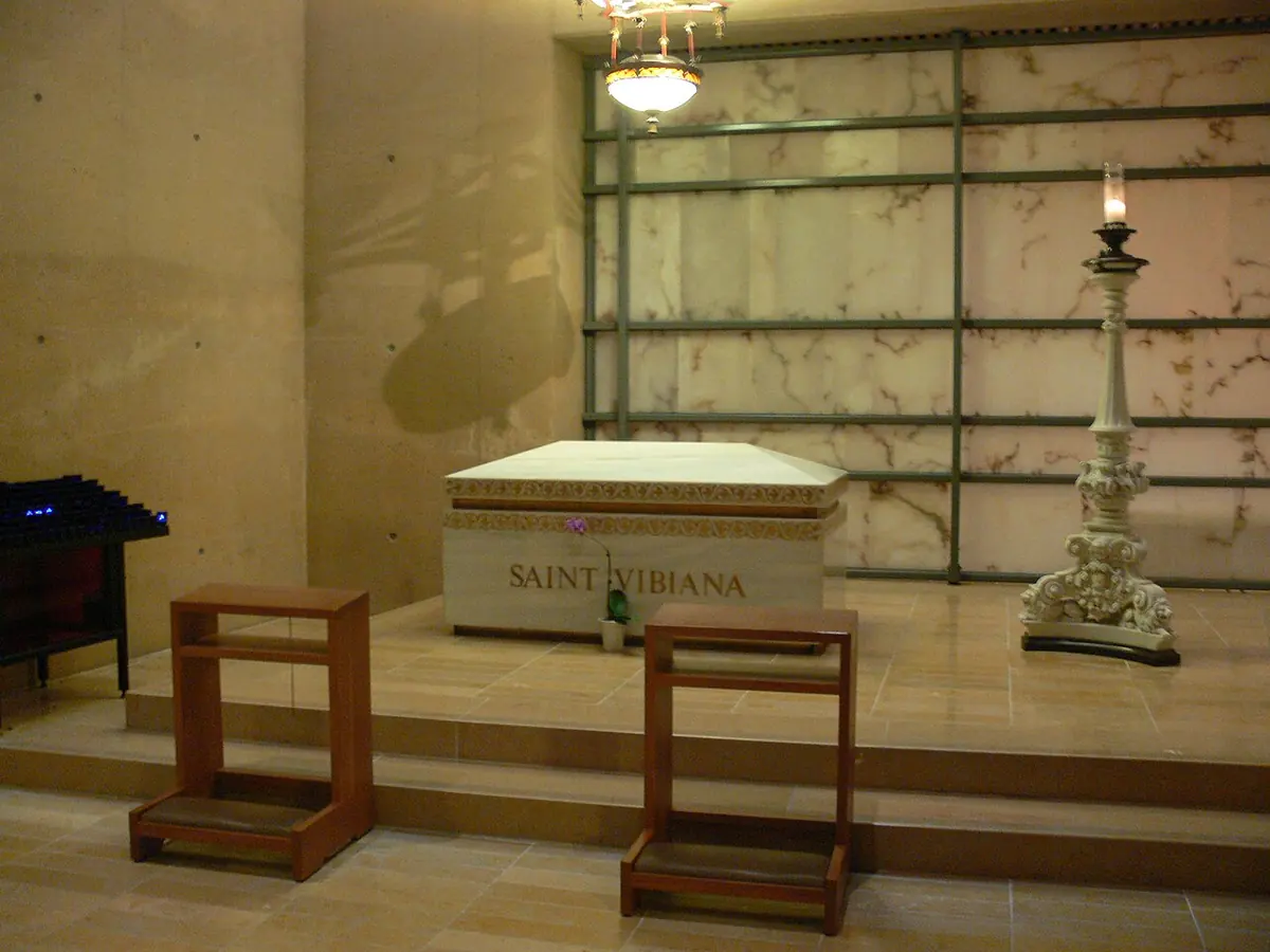 White marble sarcophagus inscribed Saint Vibiana in a quiet room of glowing alabaster panels, with two kneelers and a tall candlestick