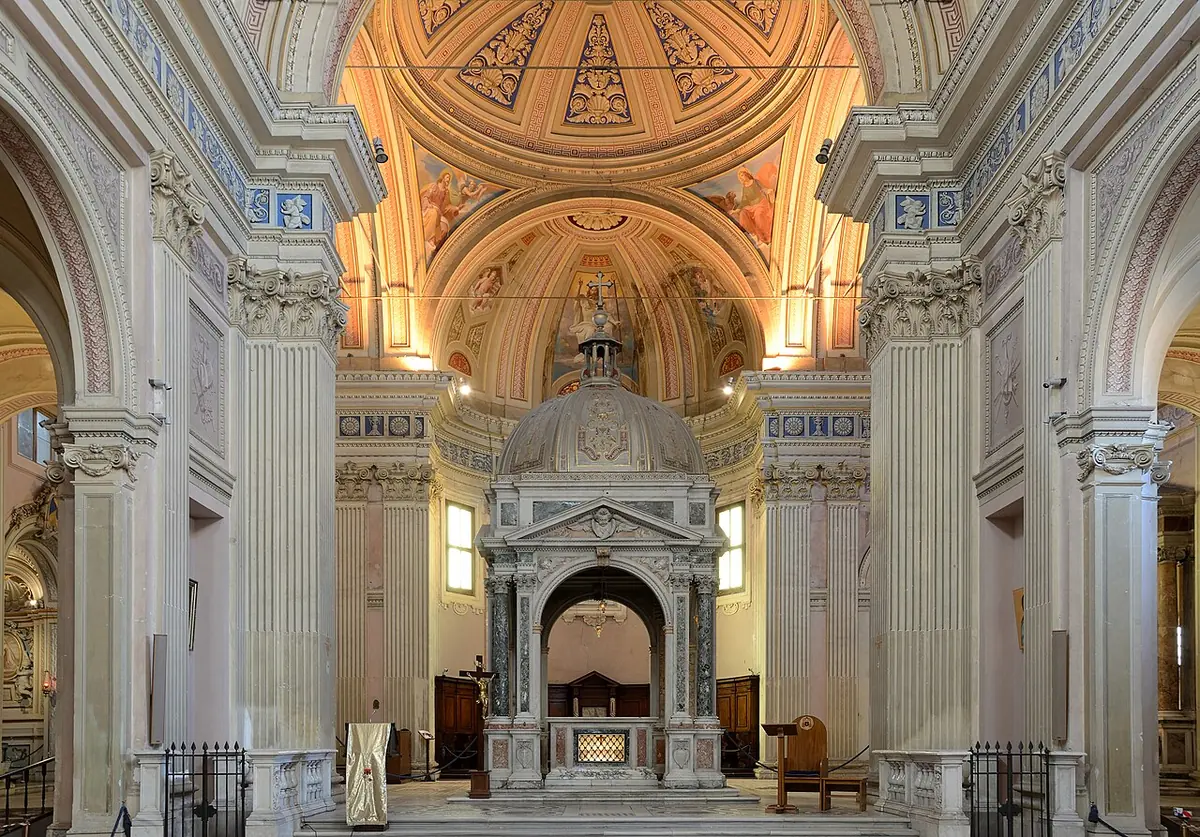 The nave of a white and gold Baroque church leading to a marble high altar under a domed canopy