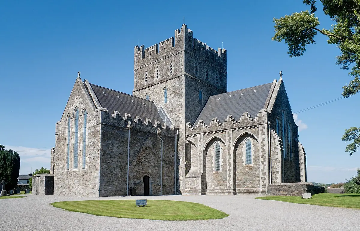 The gray stone Gothic cathedral of St. Brigid in Kildare with its square battlemented central tower, seen from the southeast under a blue sky