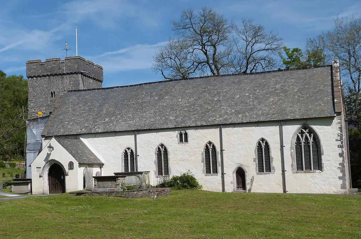 A long whitewashed stone church with a slate roof, a low square tower and Gothic windows, on a green lawn