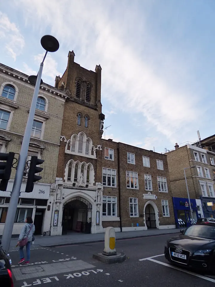 Fachada de ladrillo rojo de una iglesia neogótica victoriana con torre y entrada en arco, en una esquina de una calle de Londres