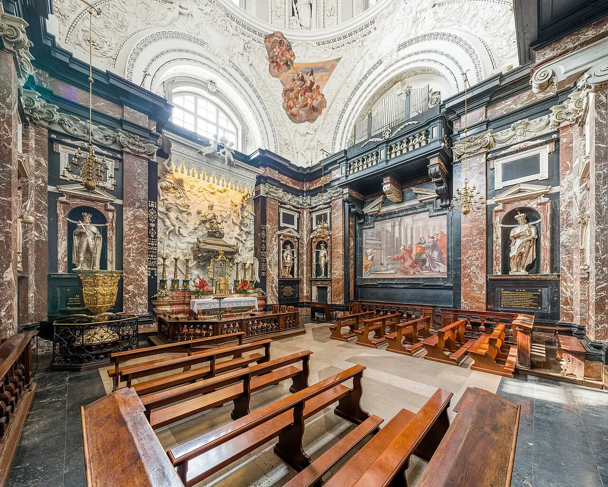 Baroque chapel lined with dark and red marble, with white stucco above, statues in niches, wooden pews and the silver sarcophagus on the altar at the far end
