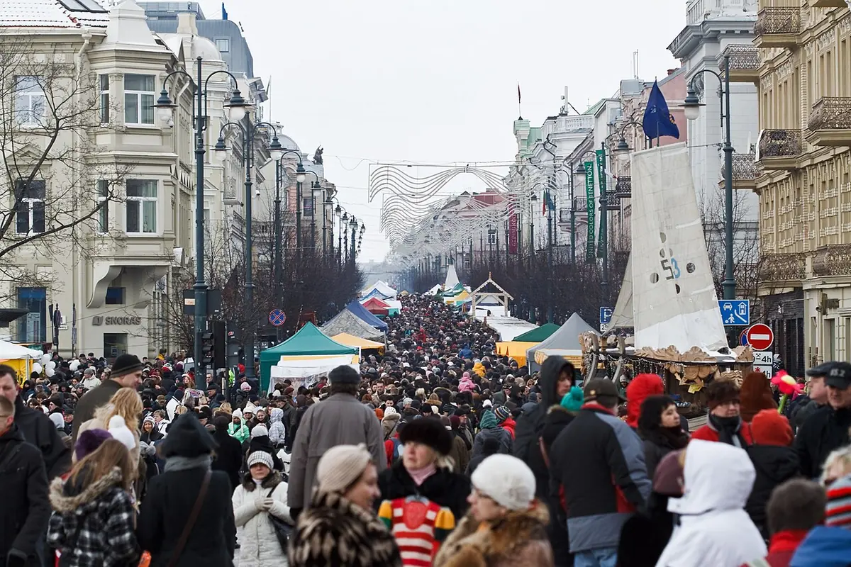 A dense crowd in winter coats and hats moving between market stalls down a long city avenue in Vilnius