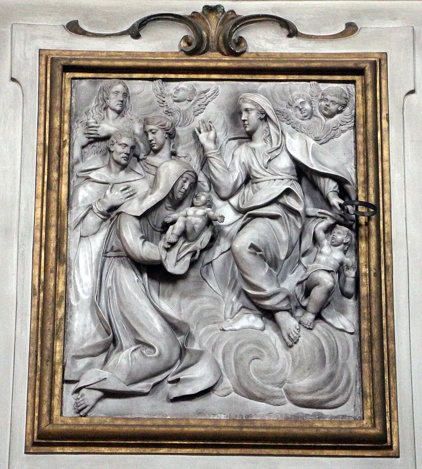 Marble relief in a gilded frame of the Virgin Mary handing the infant Jesus to a kneeling nun, with saints and angels' heads in the clouds around them