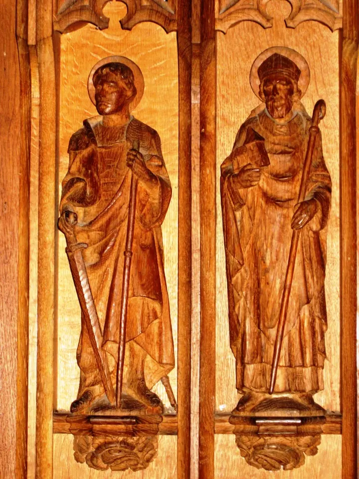 Two carved wooden figures in niches, a young soldier saint with a sword on the left and a bearded bishop with a miter and crozier on the right