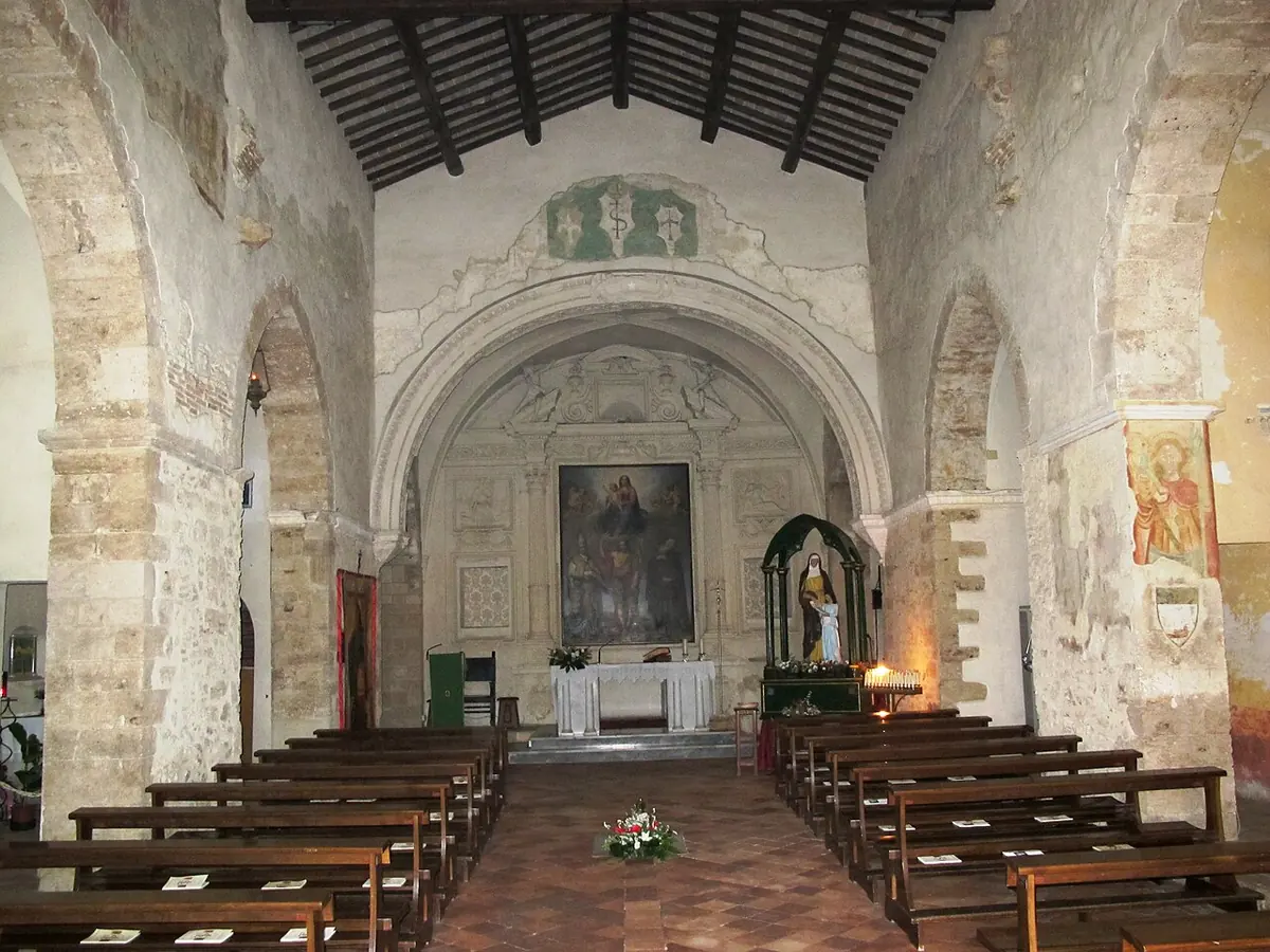 The plain stone nave of the church of Sant'Antonio in Ferentino, with wooden pews leading to an altar and a painting in the apse