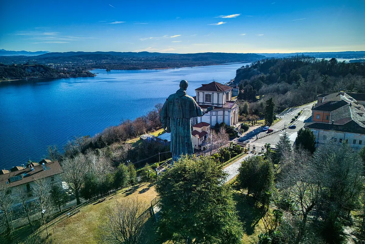 Aerial view of the giant green copper statue of St. Charles raising his hand in blessing, on a hill above the blue waters of Lake Maggiore