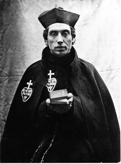 Old black-and-white photograph of a thin priest in a black biretta and black mantle with the Passionist badge on his chest, holding a small book