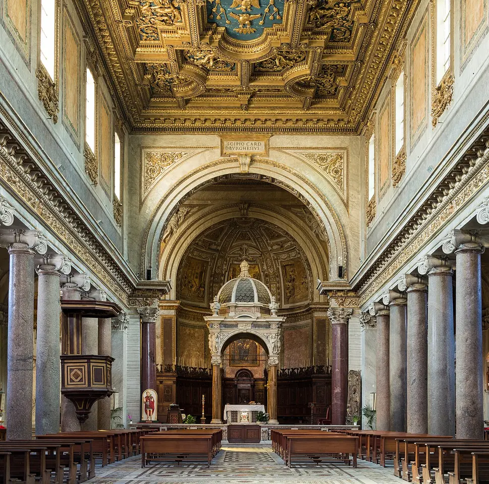 The long nave of a Roman basilica with ancient granite columns, a gilded coffered ceiling, a marble floor and a canopy over the high altar beneath a mosaic in the apse