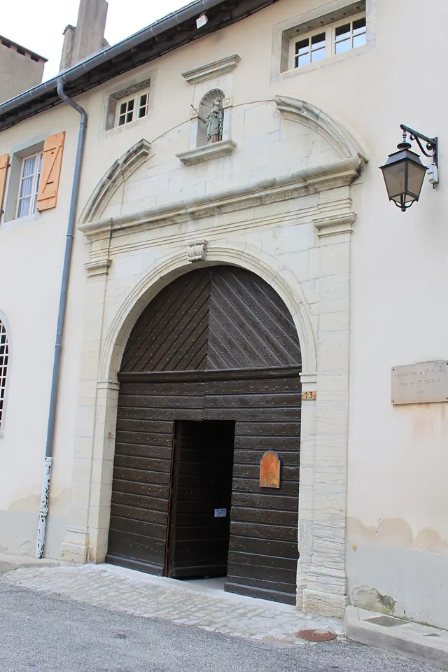 Arched wooden gate in the cream stone front of the Poor Clare monastery at Poligny, with a small statue in a niche above