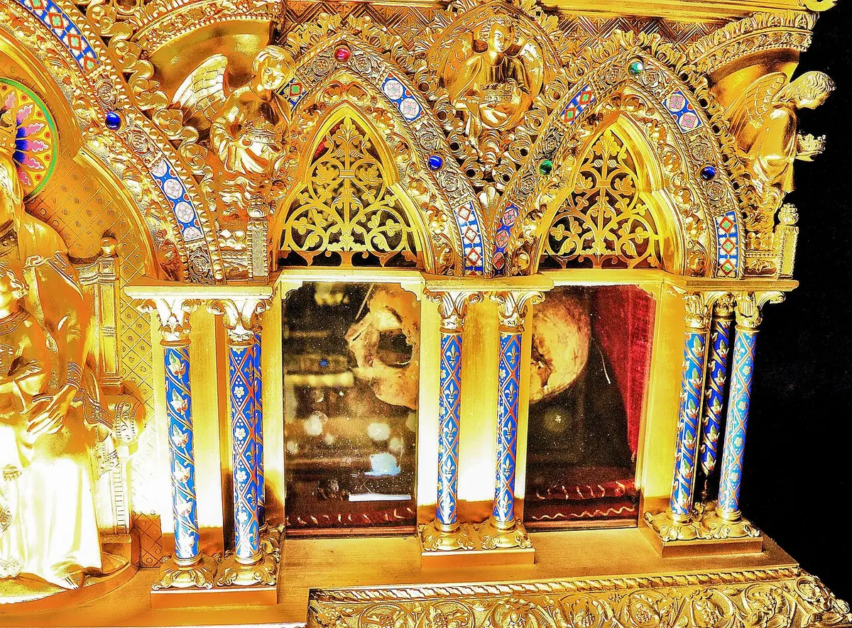 Gilded Gothic-style reliquary shrine with enamel columns, pointed arches and small statues, its glass panels showing the relics inside