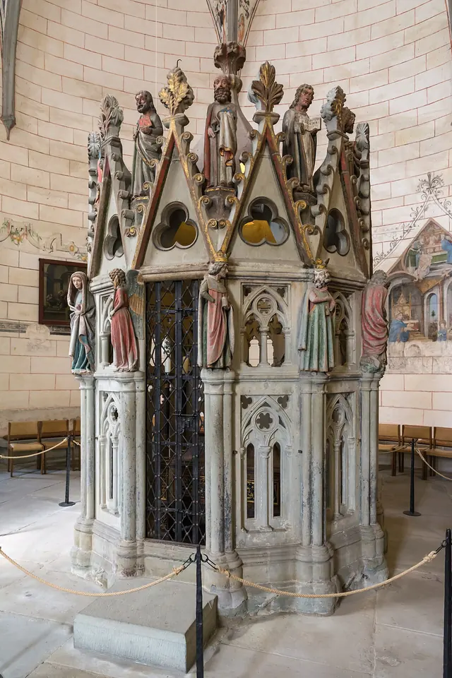 A tall Gothic stone shrine with pointed gables and painted statues, standing inside a round chapel