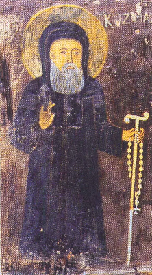 Icon of St. Cosmas in a dark monastic habit and hood, blessing with one hand and holding a staff with a prayer rope in the other