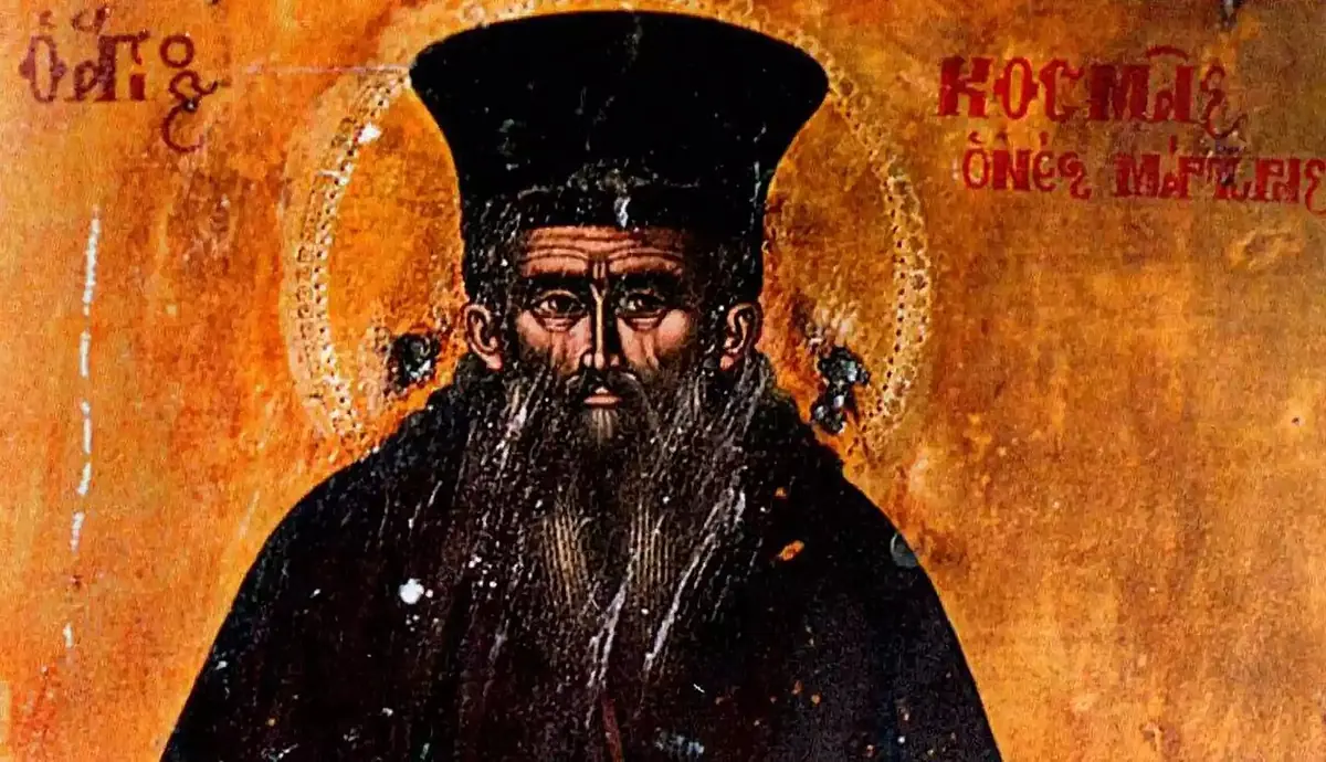 Close view of an icon of a monk with a long dark beard and a tall black cap, his halo in gold, with his name in red Greek letters