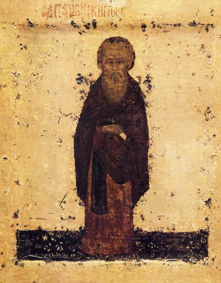 An early, worn Russian icon of an old monk with a long brown beard in a dark mantle, standing on a dark ground against a pale gold background