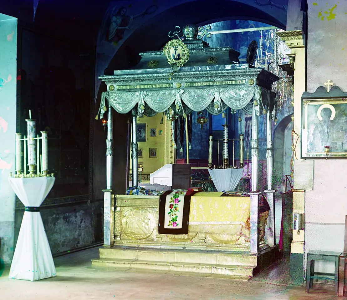 Early color photograph of a silver canopied shrine with draped fringes and candlesticks inside a dim church, with an icon on the wall at the right