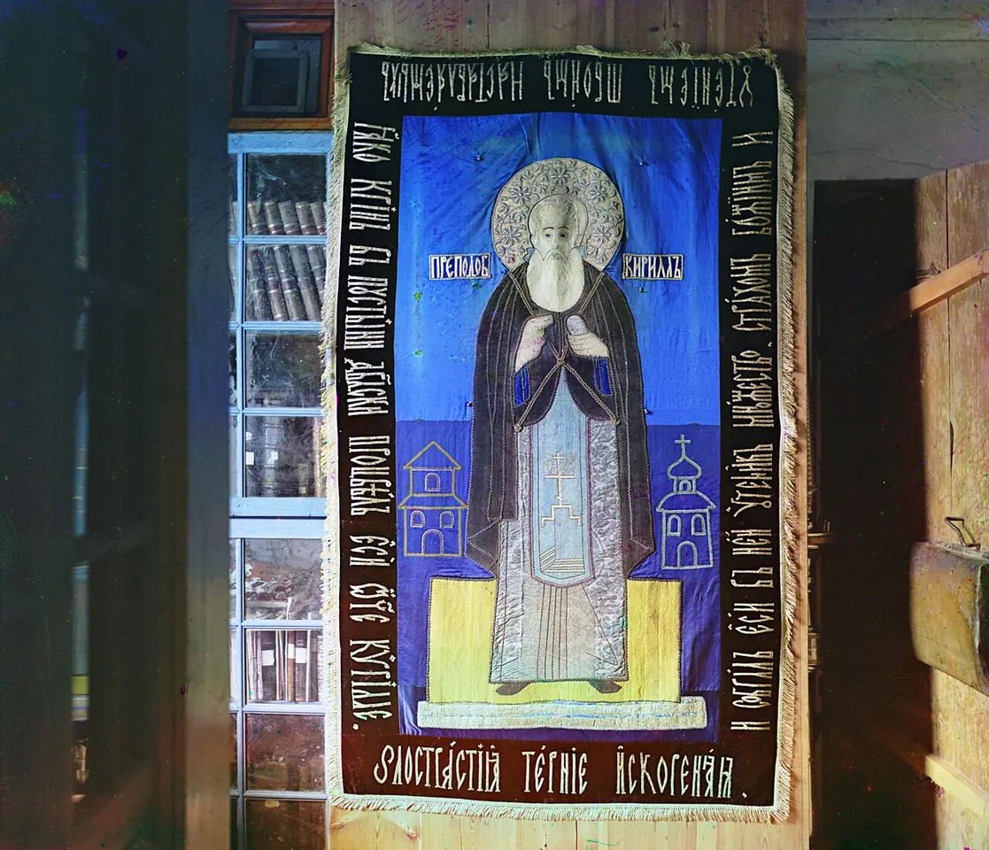 Early color photograph of a large blue embroidered cloth showing a standing monk with a halo between two small churches, bordered with lines of old Slavonic lettering