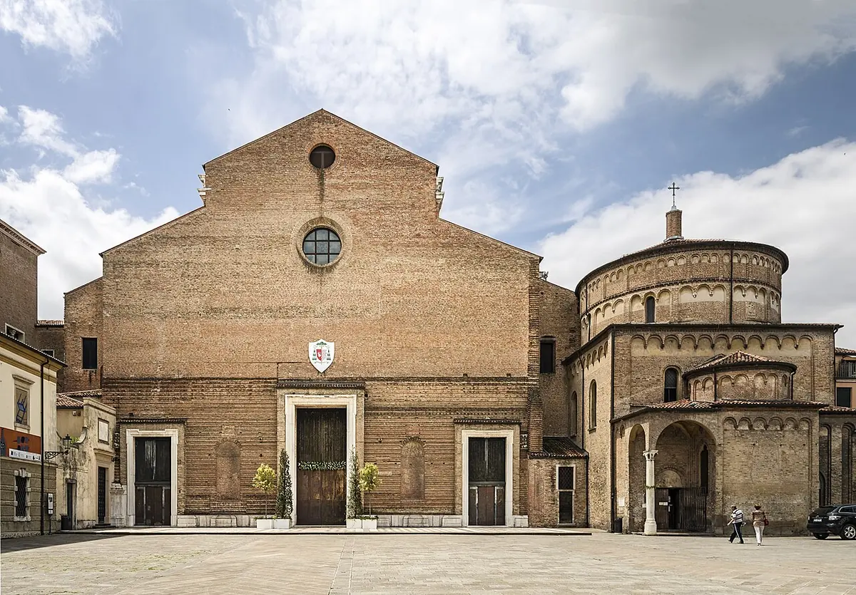 Unfinished brick facade of Padua Cathedral with three doors and a round window, beside the round domed baptistery, on an open square