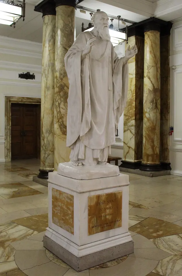White marble statue of St. David in long robes, raising one hand as he preaches, on a tall pedestal between yellow marble columns